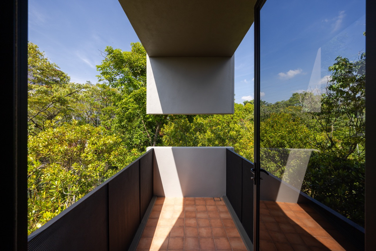 The master bedroom balcony, enclosed within the shifted upper volume, looks directly into the tree canopy that surrounds the house on three sides