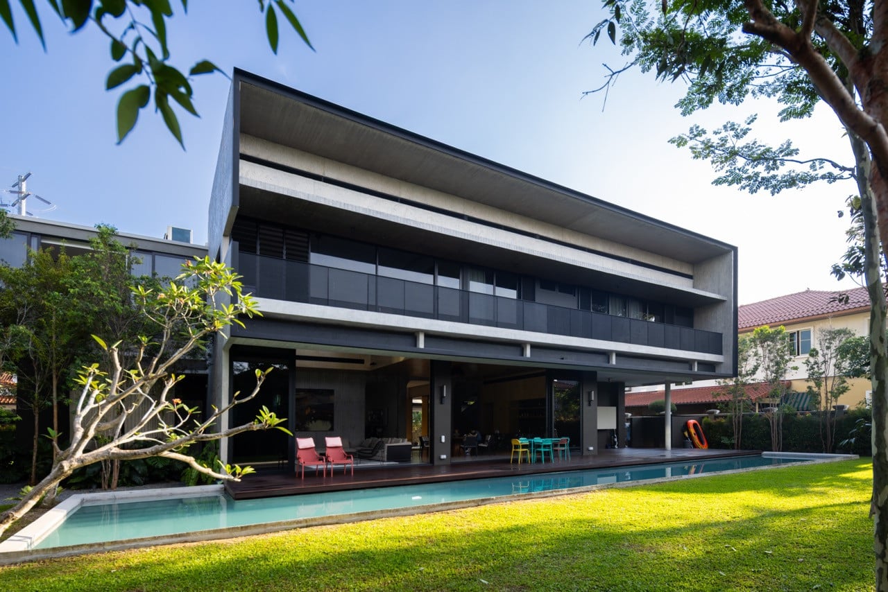 The rear facade opens fully to the pool deck and lawn, with the cantilevered upper volume providing shade to the ground-floor living spaces below