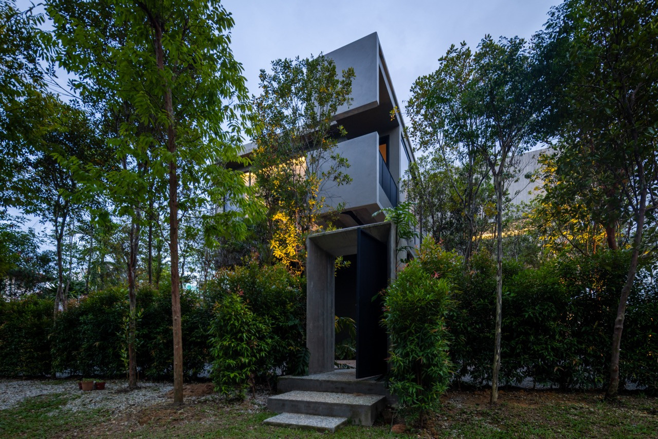 Rare trees planted in rhythmic formations by landscape contractor HJ Bina Construction SB frame the concrete volumes of Tropical Shift House at dusk