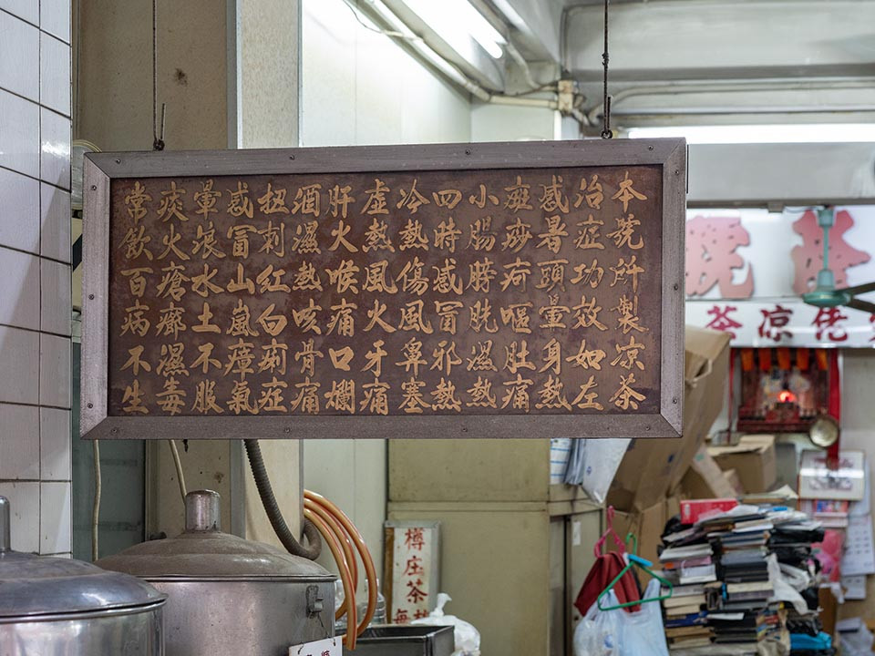 A traditional Chinese herbal tea shop displays a sign detailing ancient remedies, with fresh brews simmering below.