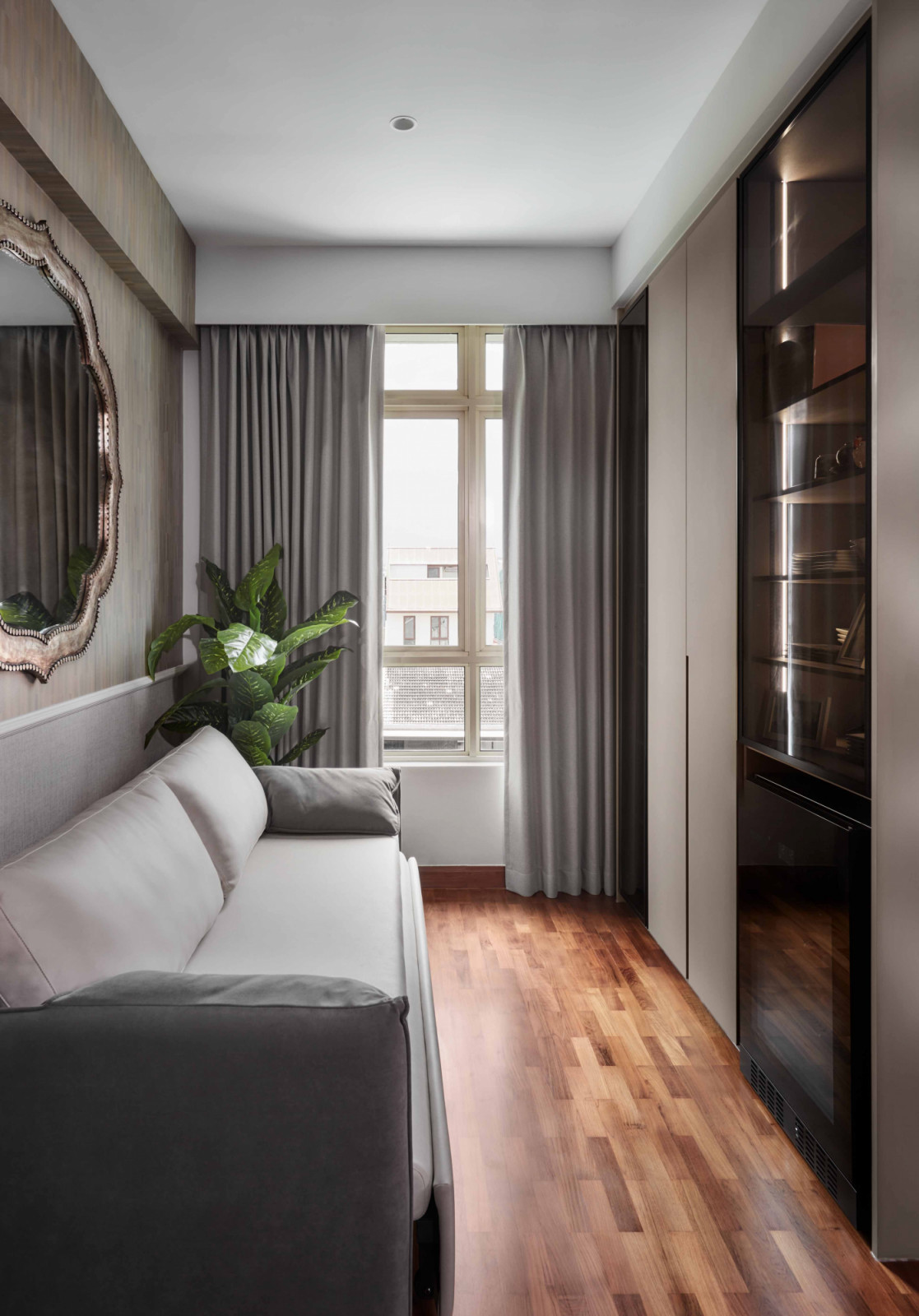 A quiet sitting nook combines soft grey upholstery with a mirrored console and built‑in wardrobe storage