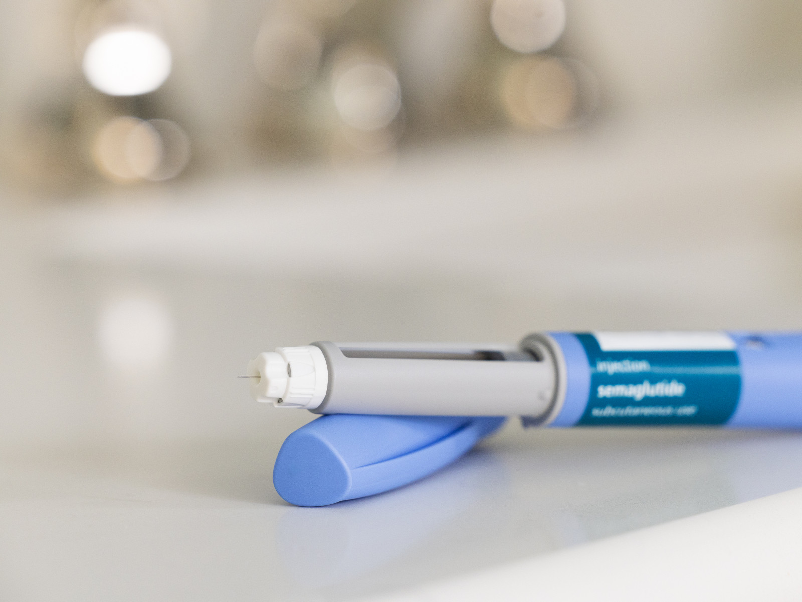 GLP-1 semaglutide injection pen, a medication used to treat Type 2 diabetes and aid in weight loss, on a white surface. The prescription medicine is used to treat Type 2 diabetes as It helps regulate blood sugar levels by stimulating insulin secretion and decreasing glucagon levels. In addition, it is also used off-label for weight loss in individuals with obesity, as it can help reduce appetite and increase feelings of fullness. The pen is positioned horizontally, with its cap removed, on a bathroom counte