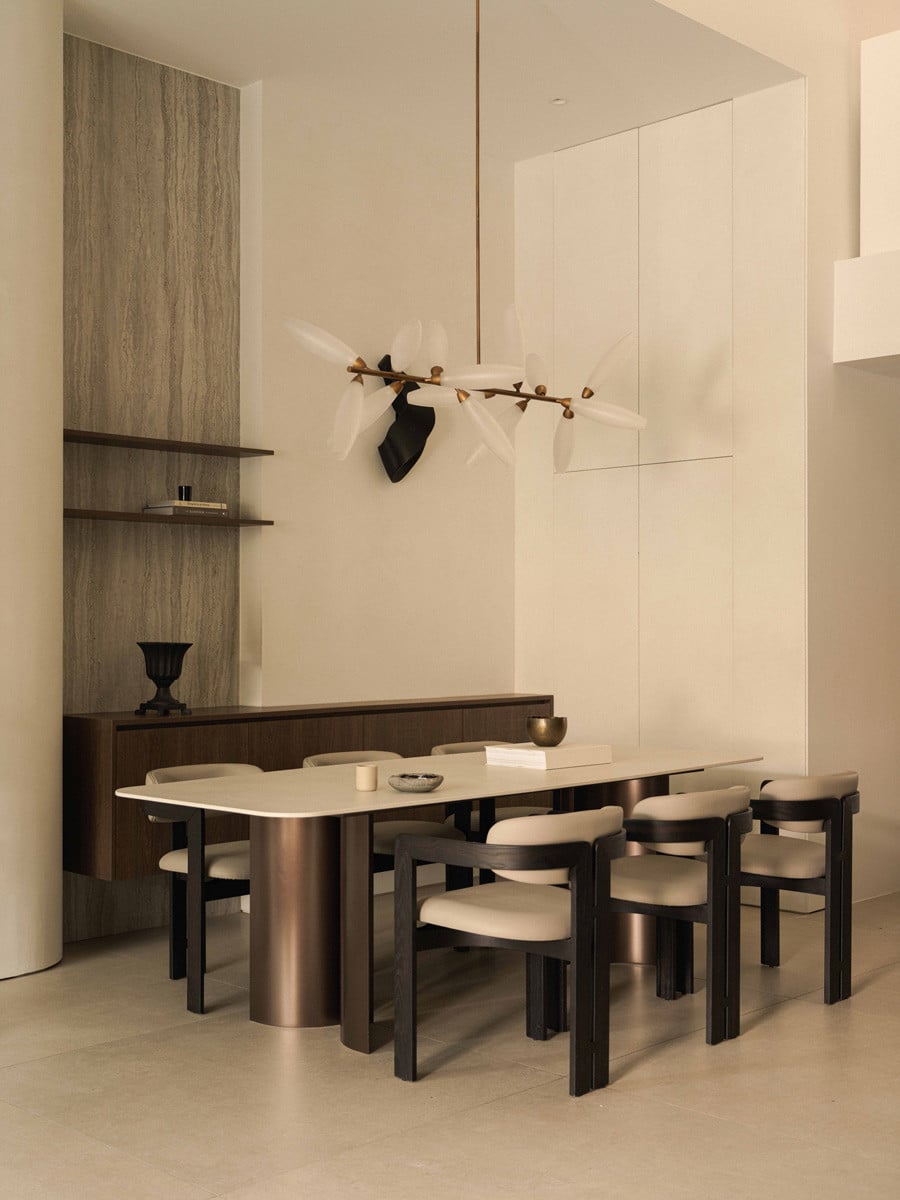 A custom dining table with curved metal legs and a Dekton surface stands beneath a sculptural chandelier in the terrace house’s dining room