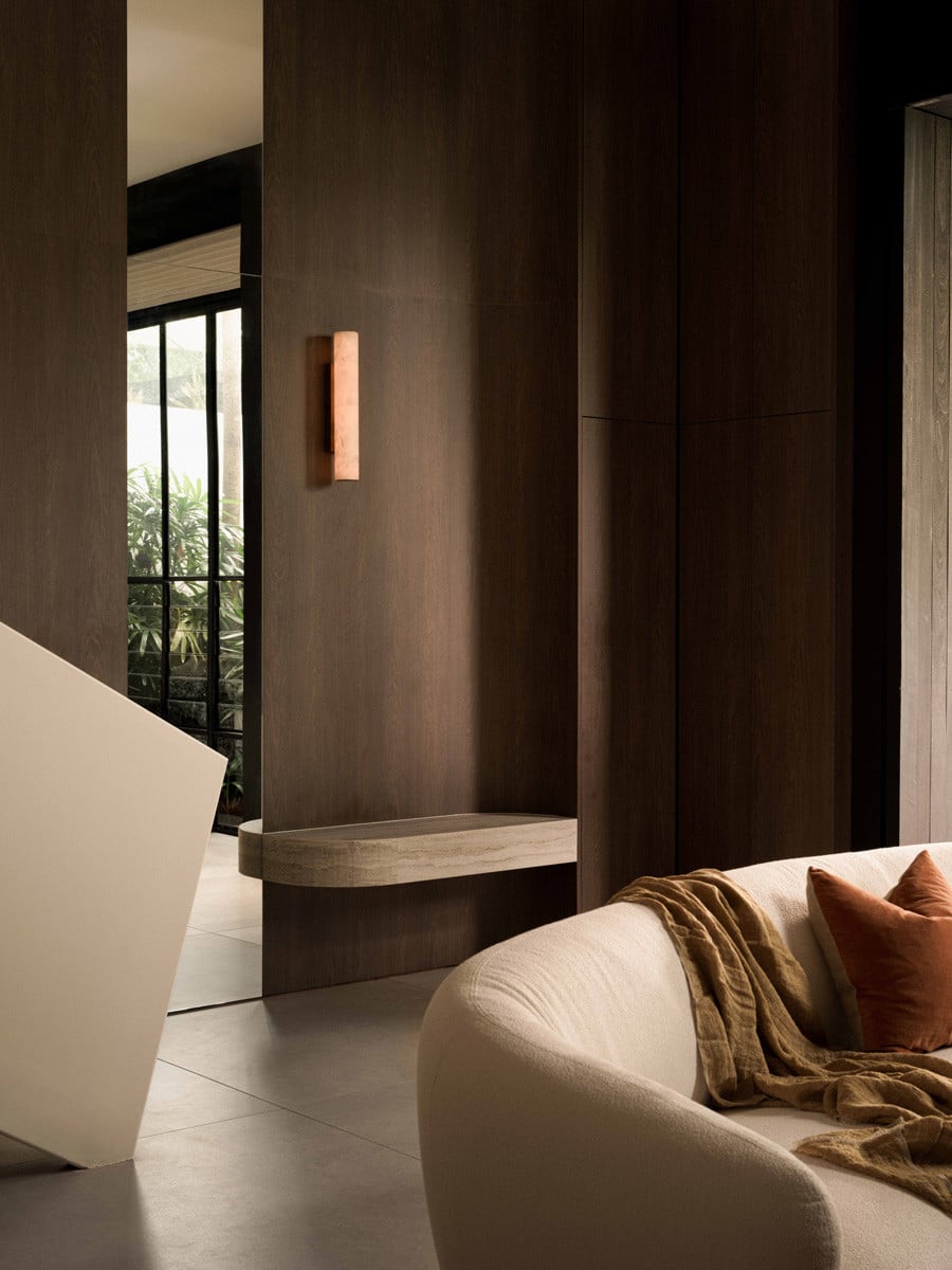 A travertine bench built into the dark wood panelling offers a quiet pause, with greenery visible through the steel-framed window beyond
