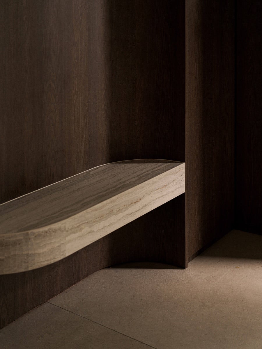 A closer look at the travertine bench, its curved form softening the run of dark wood panelling