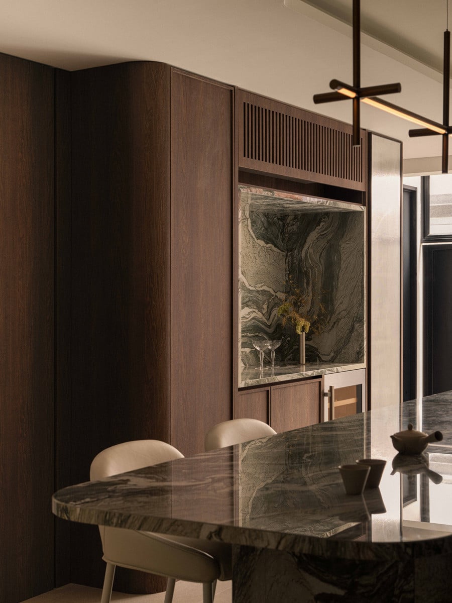 A marbled stone backsplash and curved wood cabinetry frame this quiet corner of the terrace house’s kitchen