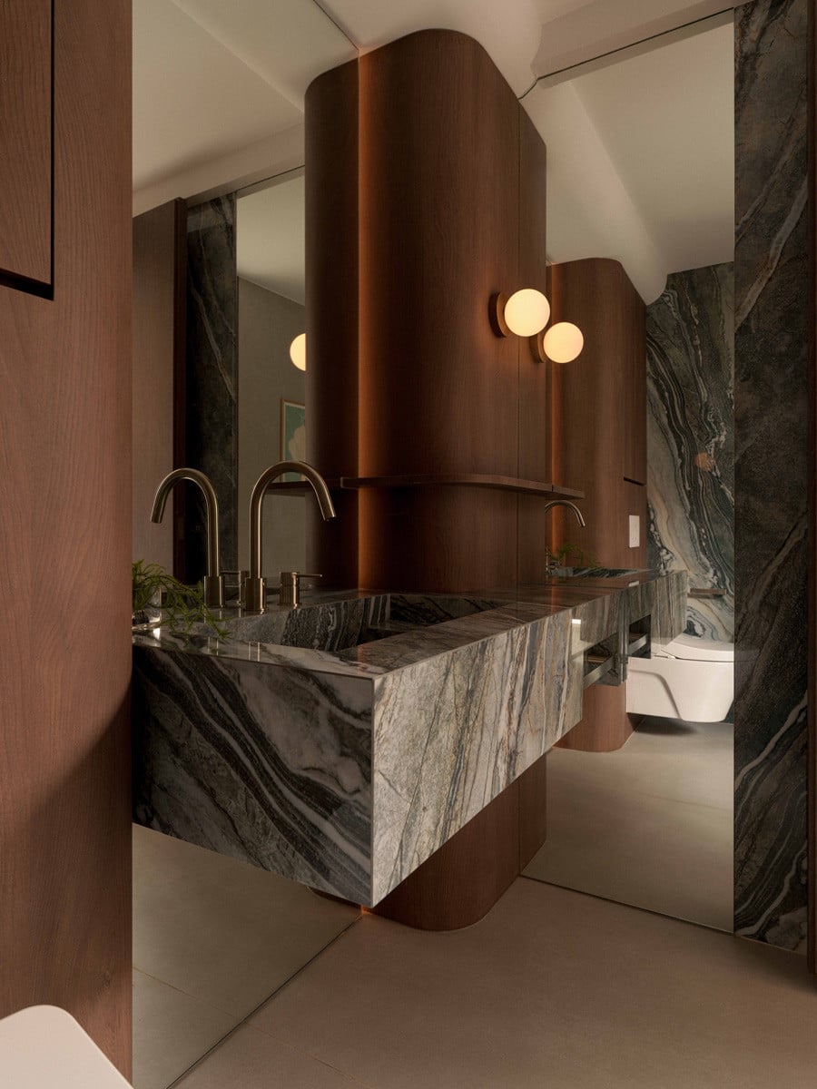Large-format Reves Blue Onyx porcelain from Florim wraps the vanity, set against curved timber volumes and globe sconces