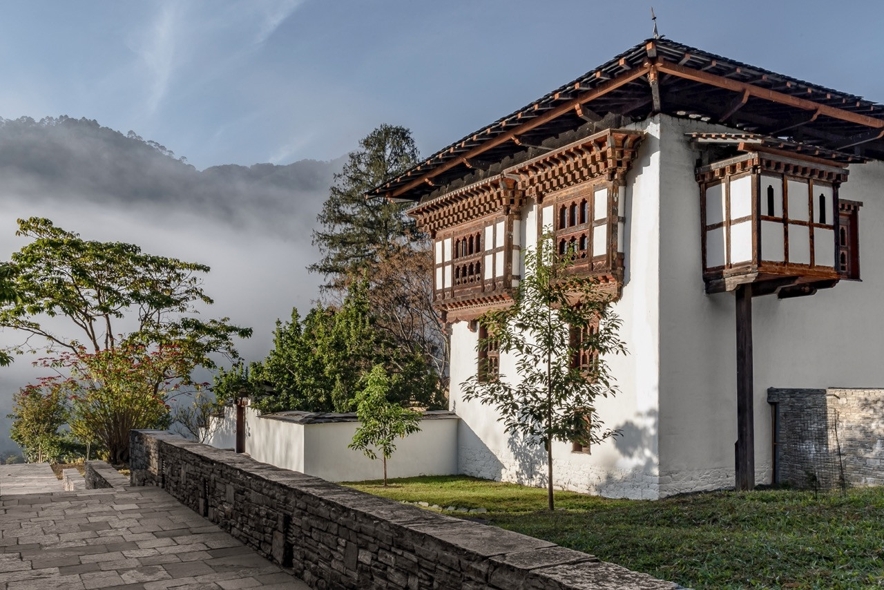 Amankora Punakha Lodge occupies a whitewashed traditional farmhouse with carved timber window frames and a projecting upper balcony