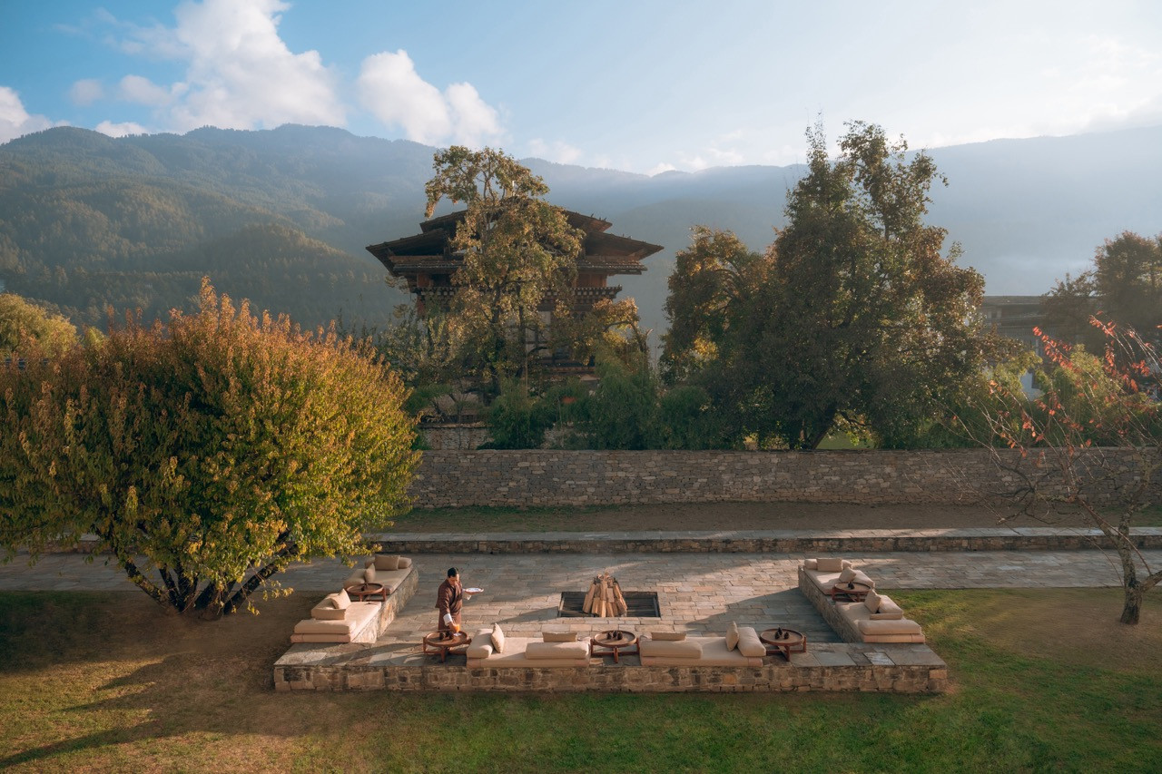 A sunken stone firepit lounge at Amankora Bumthang Lodge looks out toward Jakar Dzong at golden hour