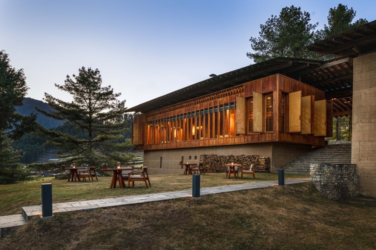 Amankora Gangtey Lodge’s timber-clad guest pavilion glows at dusk with outdoor firepit seating overlooking the Phobjikha Valley
