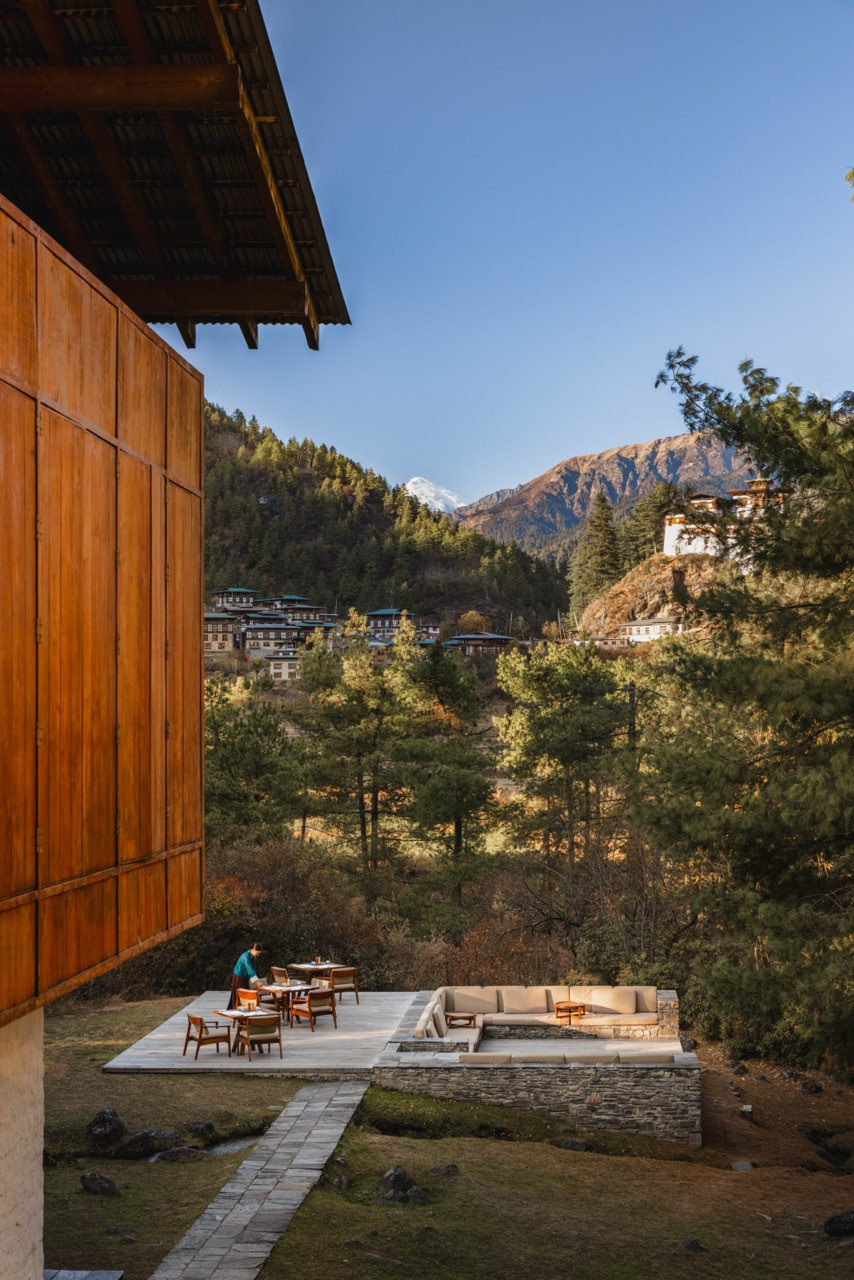 Amankora Paro Lodge’s terrace and firepit seating overlook the village below with Drukgyel Dzong and a snow-capped peak in the distance