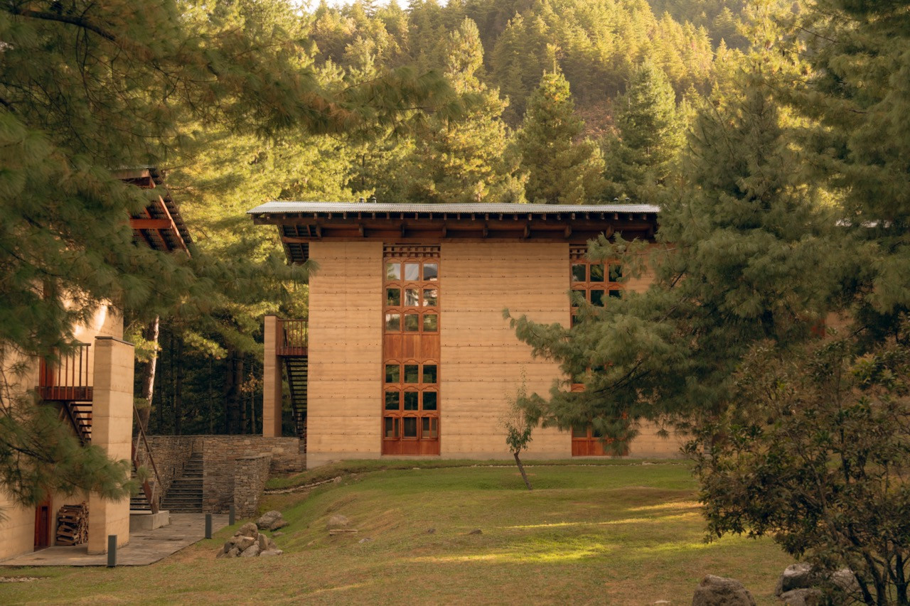 The stabilised rammed-earth facade of an Amankora Paro Lodge suite building sits framed by pine forest