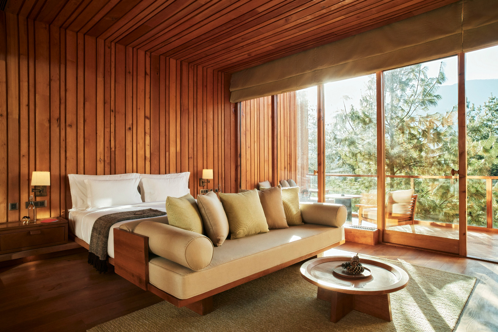 A suite bedroom at Six Senses Bumthang pairs timber panelling with a daybed positioned to look onto the surrounding pine forest