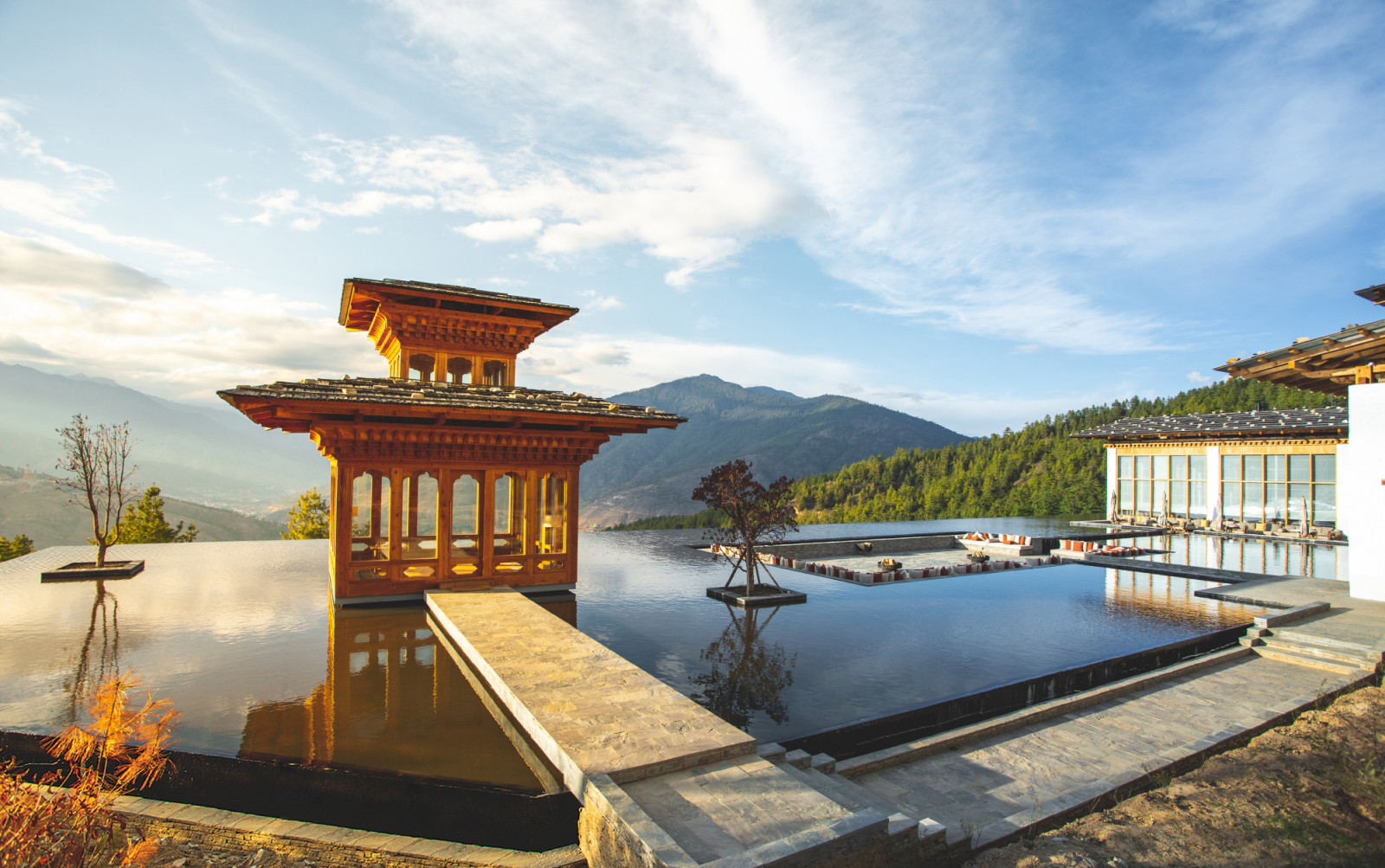 A prayer pavilion floats on the reflecting pools of Six Senses Thimphu with the Paro Valley and surrounding mountains beyond