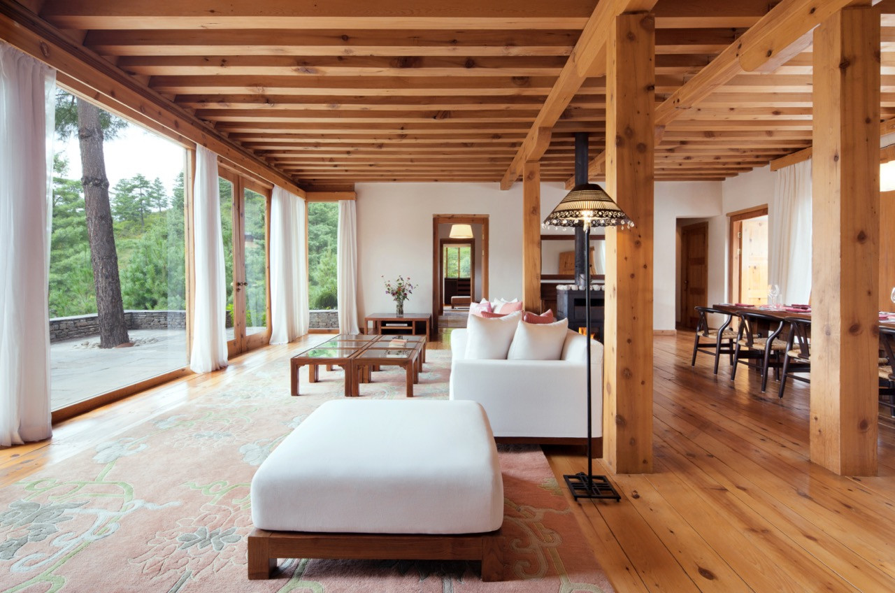 A one-bedroom villa living room at Uma Paro pairs exposed timber beams with pale furnishings and full-height glass doors onto the garden