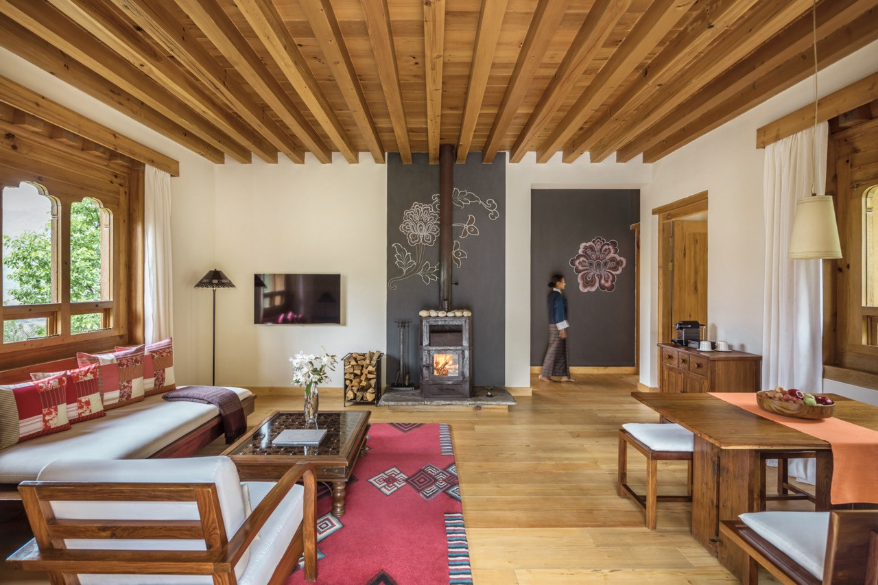 A villa living area centres on a wood-burning stove against a hand-painted wall, with a dining table set beneath the timber-beamed ceiling