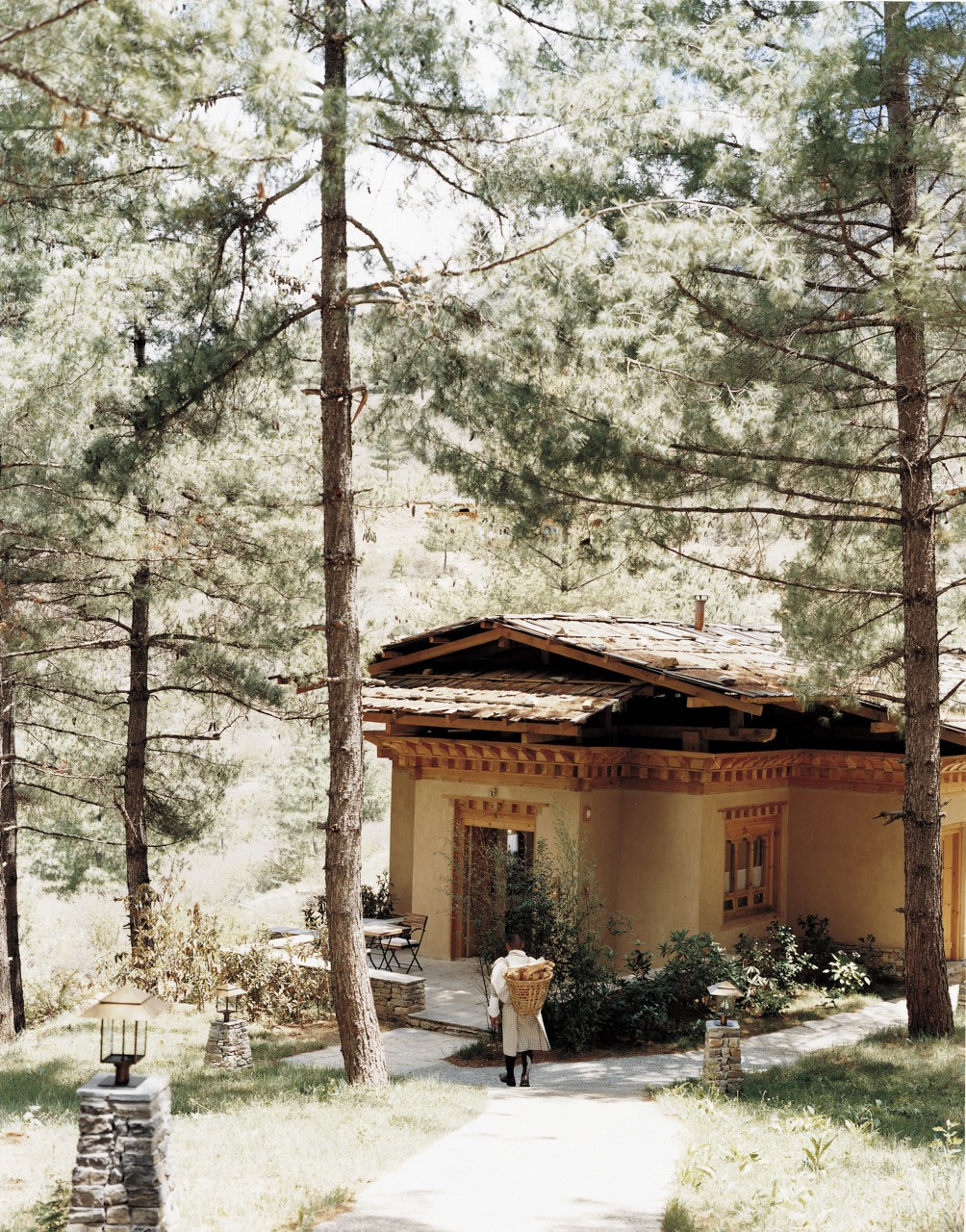 A guest villa at Uma Paro sits among pine trees, its ochre walls and shingled roof reached by a stone path