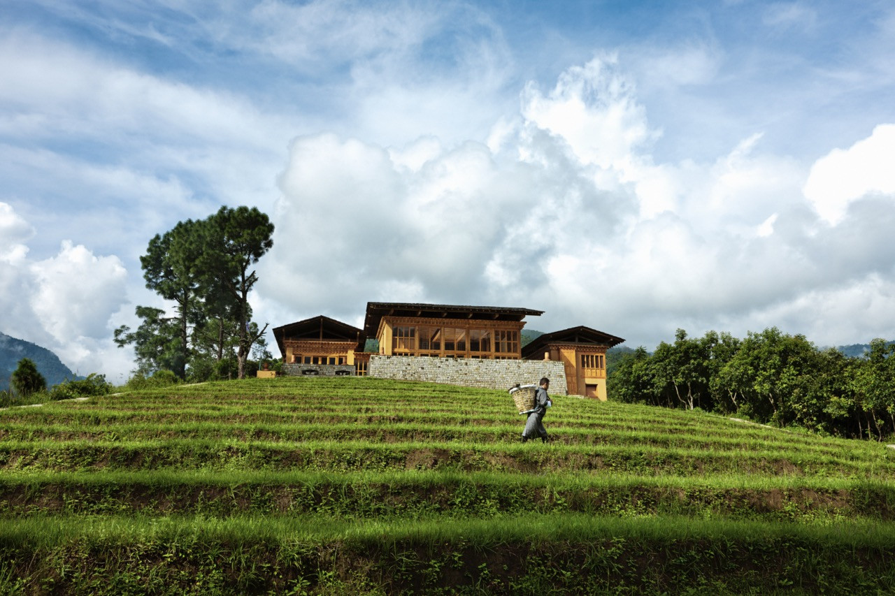 Uma Punakha’s main lodge sits above terraced rice fields, with a farmer crossing the paddy in the foreground