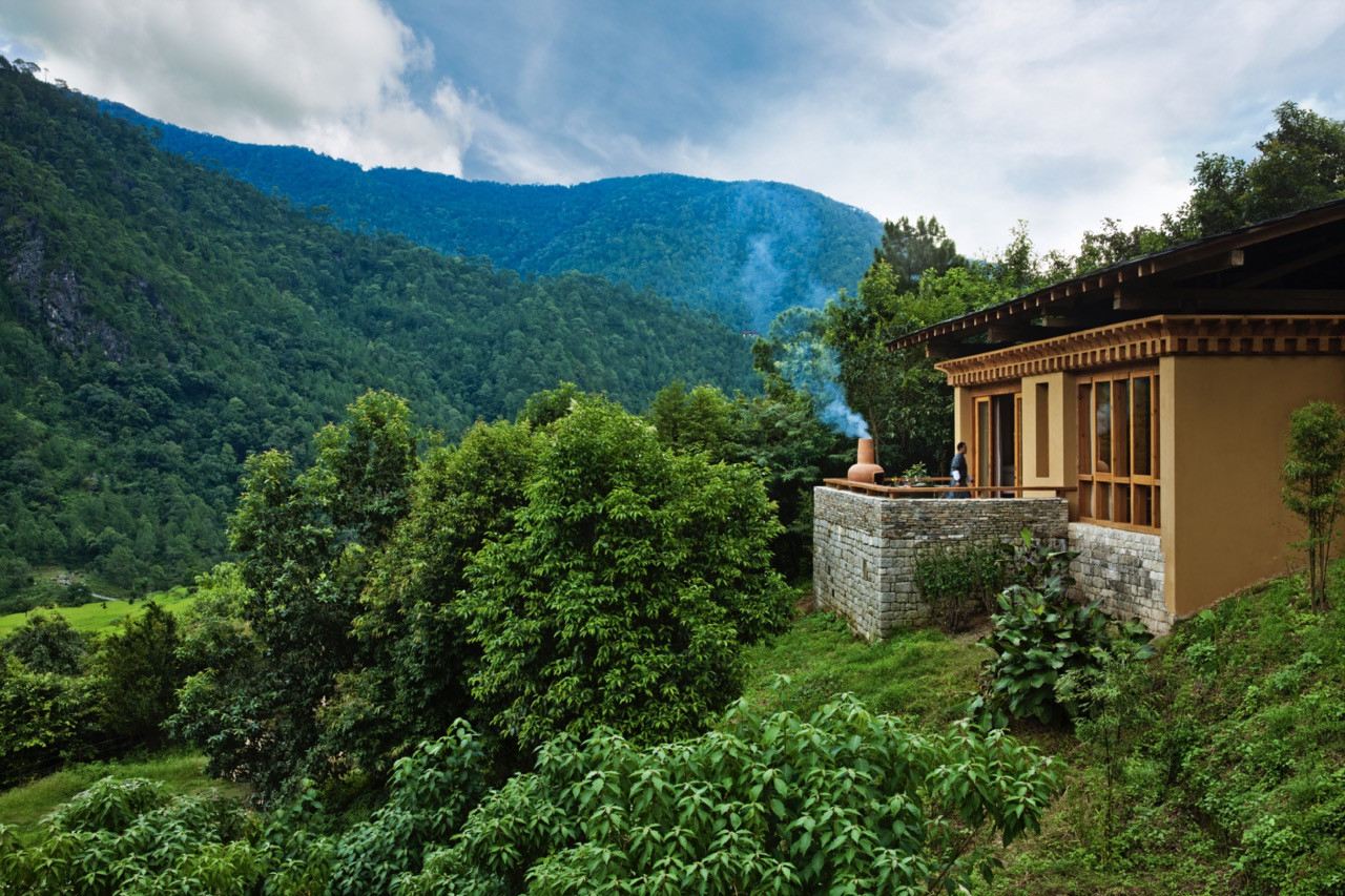 A villa terrace at Uma Punakha overlooks the forested Mo Chu valley, with a traditional clay incense burner sending up smoke