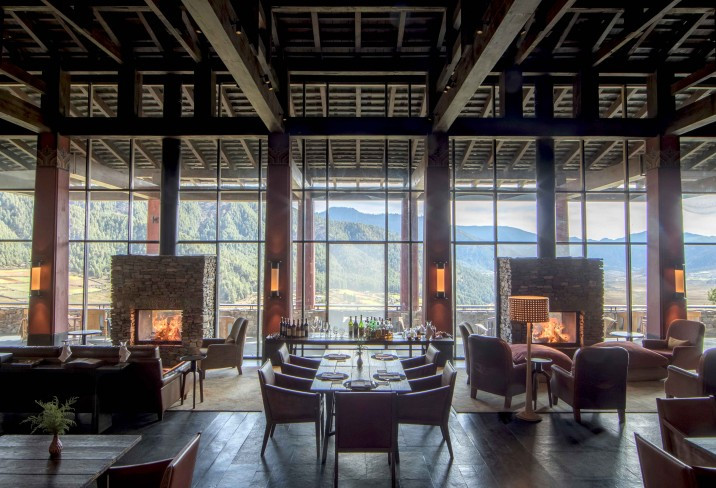 Gangtey Lodge’s double-height lounge centres on twin stone fireplaces beneath a soaring timber-beamed ceiling, with floor-to-ceiling glass onto the valley