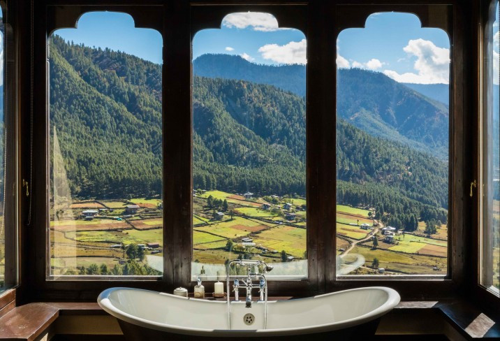 Arched windows above a freestanding bathtub at Gangtey Lodge look out over the farmed valley floor and forested hills
