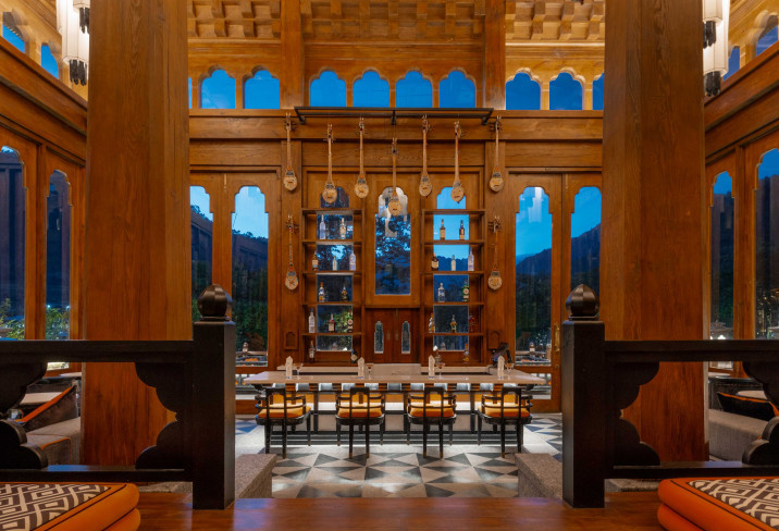 Carved timber archways and hanging shoulder bags frame the bar at Pemako Punakha, styled in Bill Bensley’s maximalist take on dzong architecture