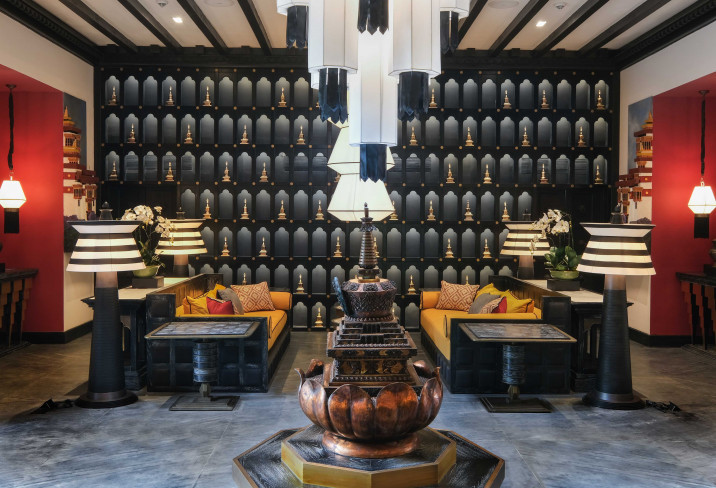 A lounge at Pemako Punakha centres on a copper lotus fountain beneath a wall of stacked prayer-wheel motifs and striped pendant lamps