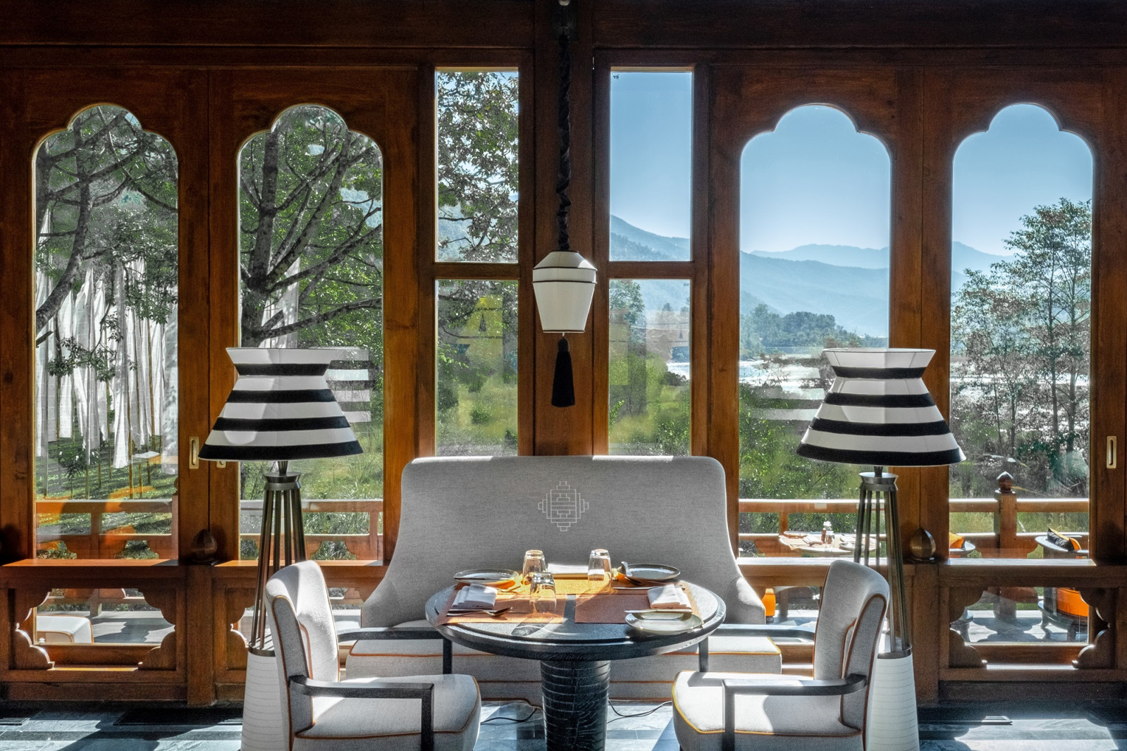 Bill Bensley’s arched windows and striped Ara Bar lamps frame the Mo Chu River at Pemako Punakha’s restaurant