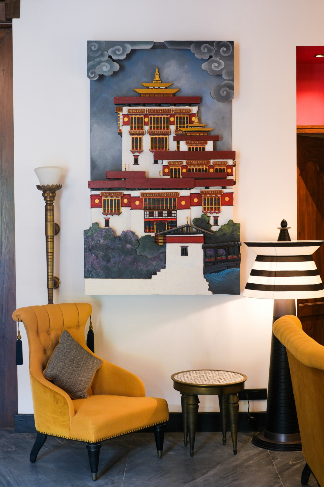 A hand-painted dzong relief hangs above mustard-yellow armchairs in a Pemako Punakha lounge, styled with Bensley’s signature striped lamps