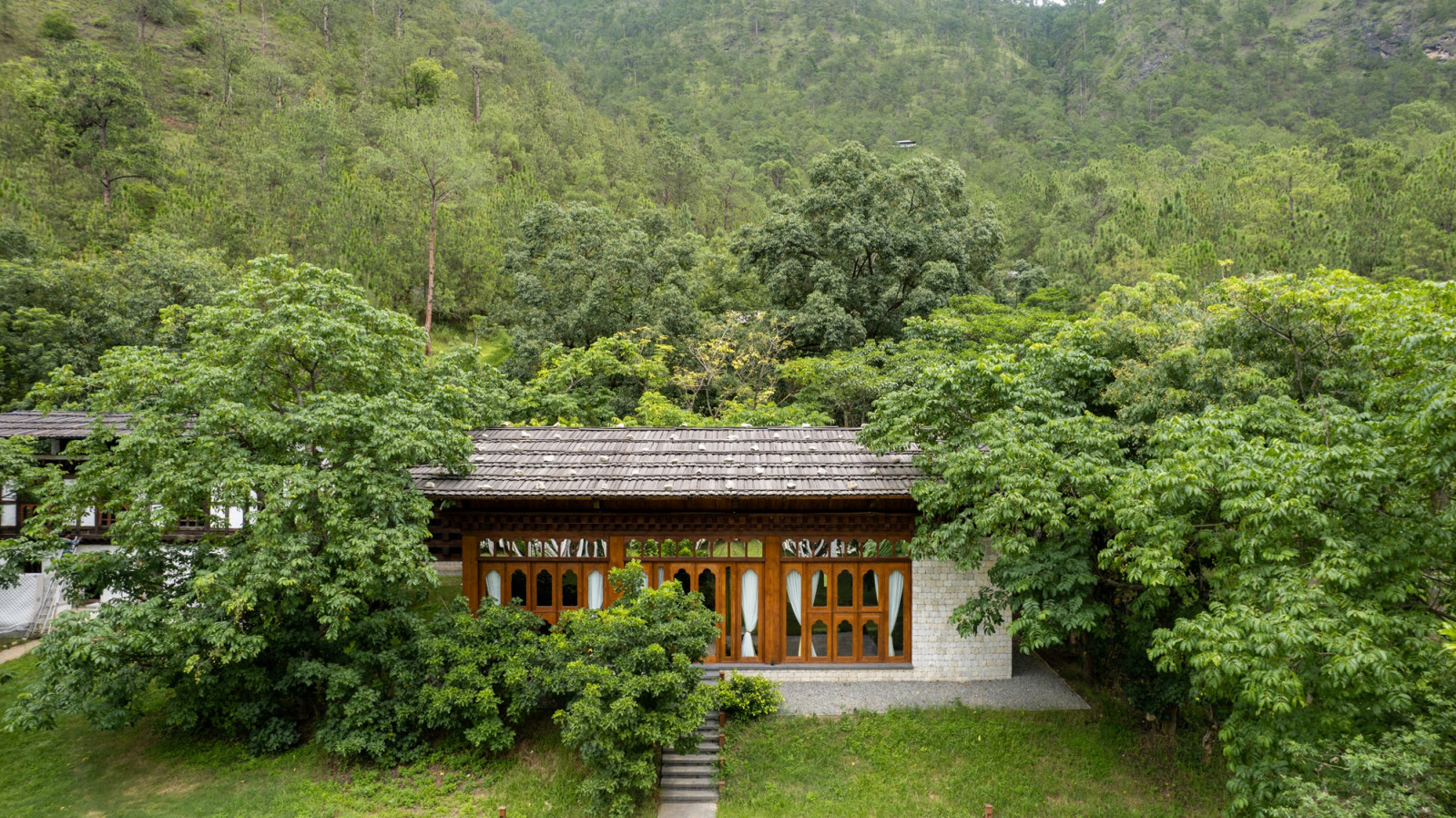 A tented villa at Pemako Punakha sits screened by trees, its arched timber windows and stone base echoing dzong construction