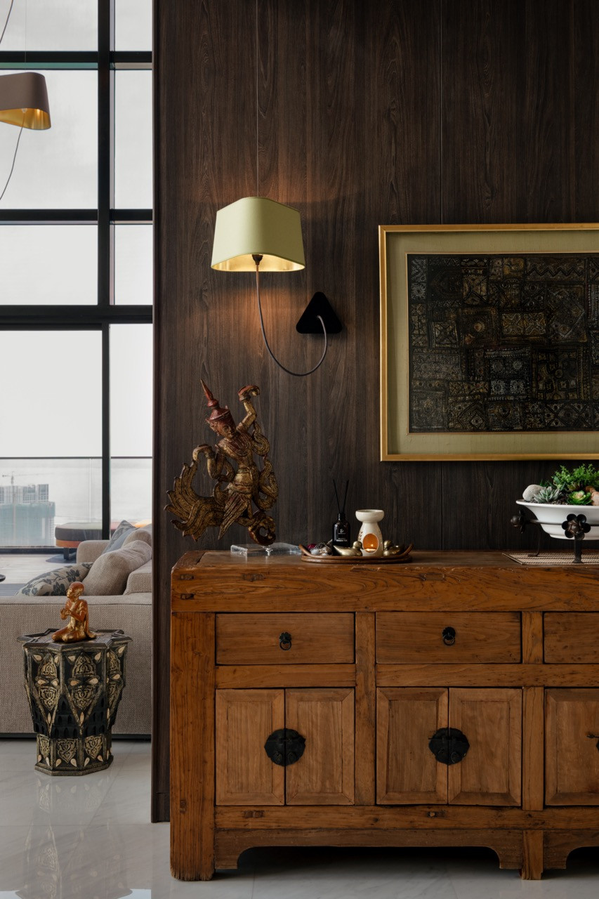 Against dark timber wall panelling, a reclaimed wooden sideboard displays objects gathered from the clients’ travels across Southeast Asia