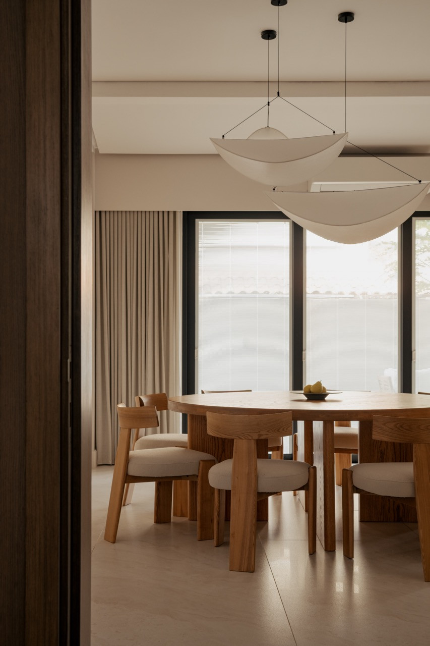 The dining table, in solid timber with a rounded top, sits beneath a pair of crescent-shaped pendant lights
