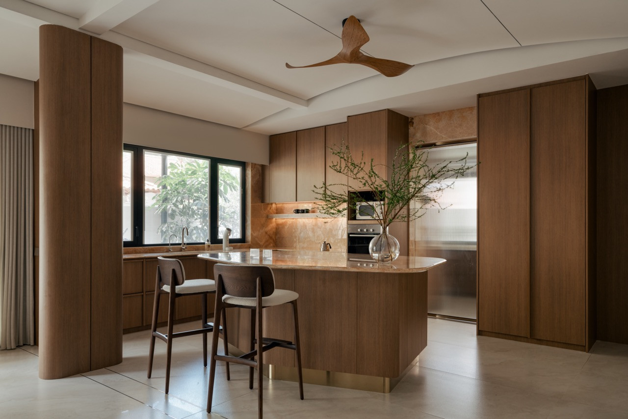 The wet kitchen island, topped in the same onyx marble, is flanked by a pair of timber counter stools beneath a sculptural wooden ceiling fan