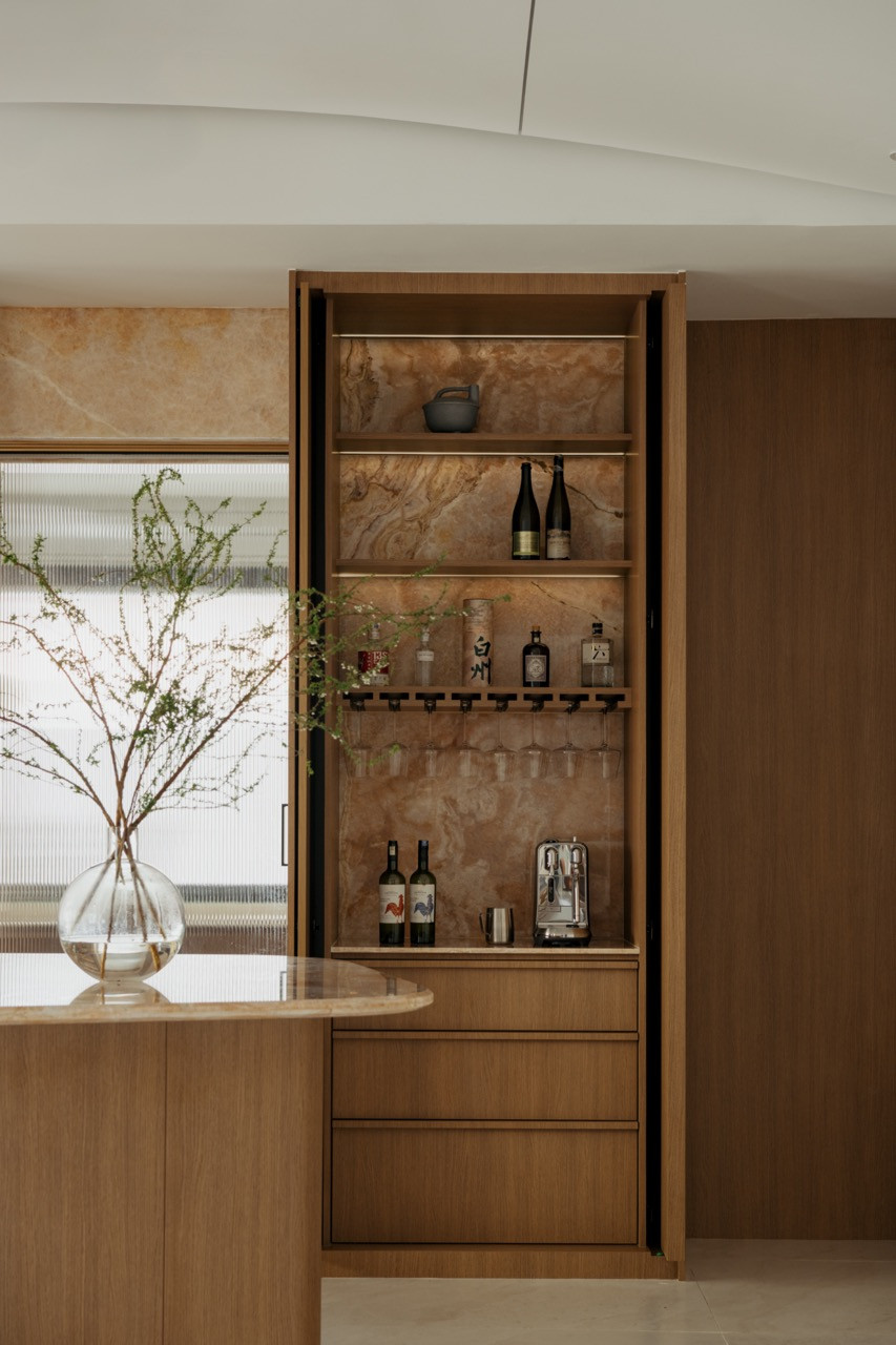 A concealed bar cabinet opens to reveal a stone-lined interior stocked with spirits, wine, and glassware