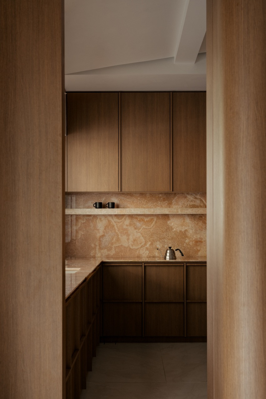 A dry kitchen counter is finished in book-matched onyx, with a stovetop kettle and a pair of mugs set on open shelving