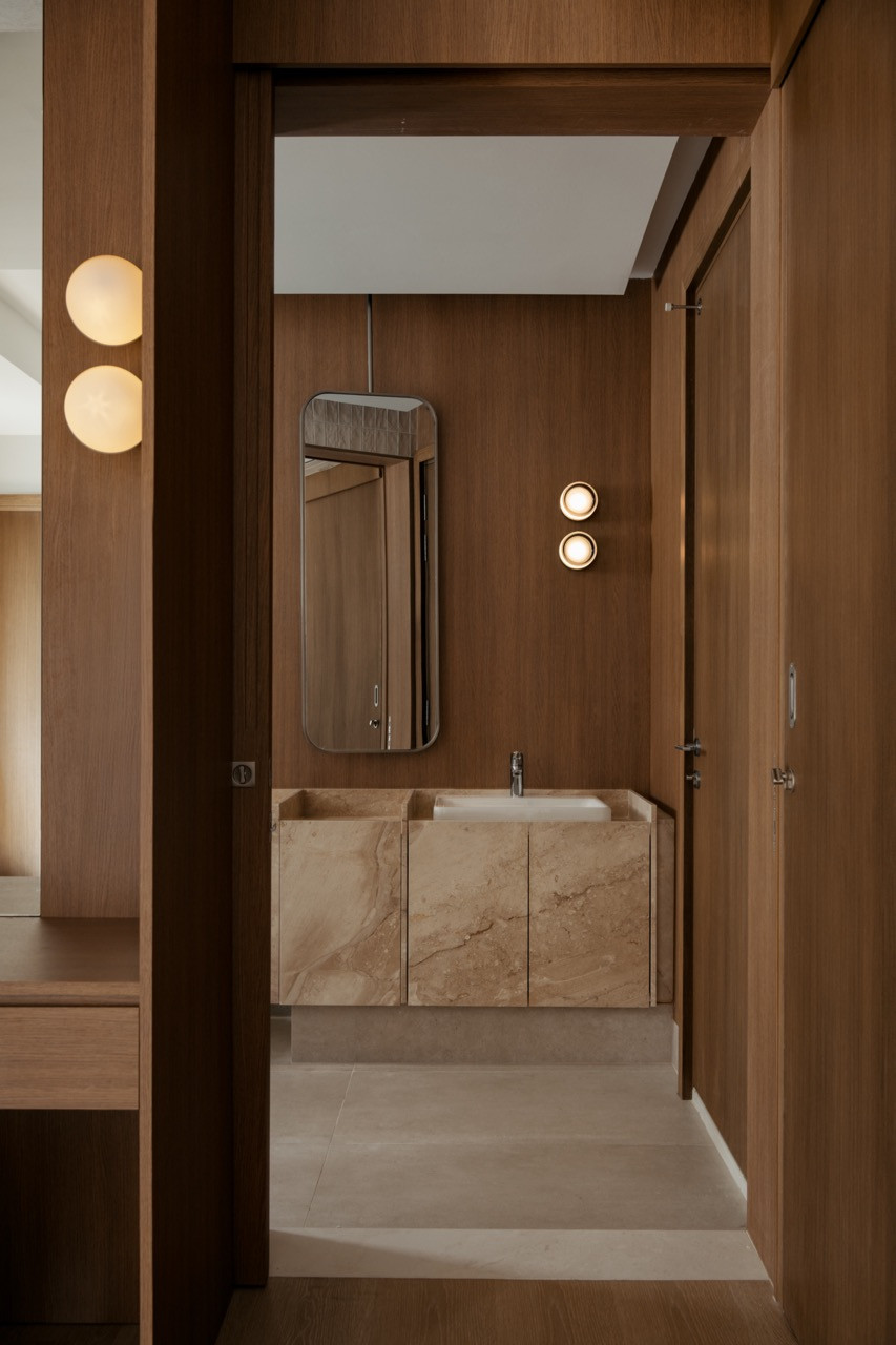 A further bathroom entrance reveals a marble vanity beneath a pill-shaped mirror, flanked by twin wall sconces