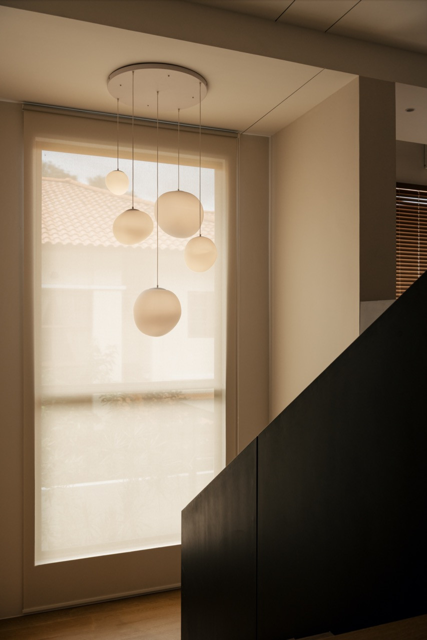 A cluster of spherical pendant lights hangs above the staircase landing, positioned against a sheer-curtained window