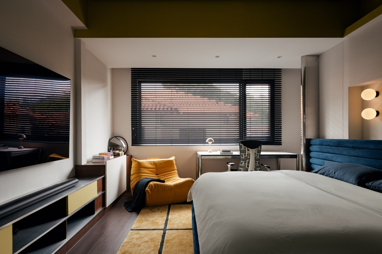 A guest bedroom takes a bolder turn, with a navy channel-tufted headboard, mustard armchair, and an olive-toned ceiling.
