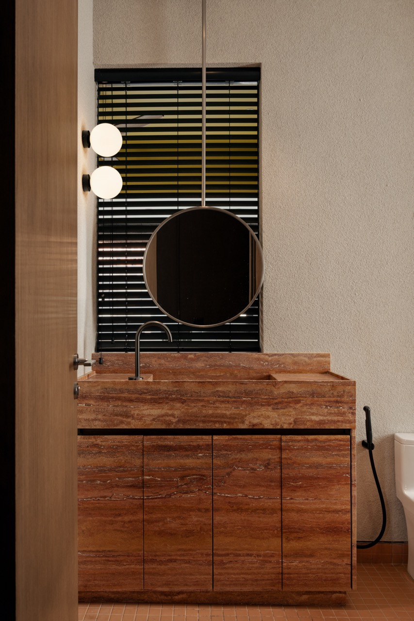 The powder room vanity is clad in travertine, paired with a round mirror and twin globe sconces set against a textured wall