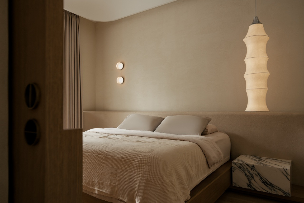 In the bedroom, a fabric pendant lamp and twin wall sconces frame the headboard wall, with a marble side table set against the timber bed base