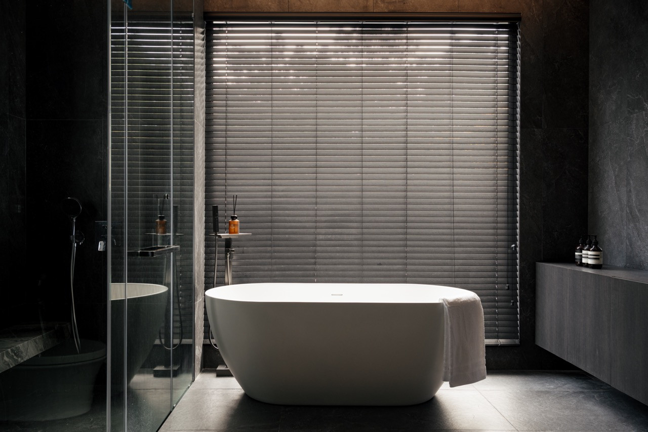 The primary bathroom pairs a freestanding tub with dark stone surfaces and timber blinds, the material palette shifting to a moodier register than the rest of the home