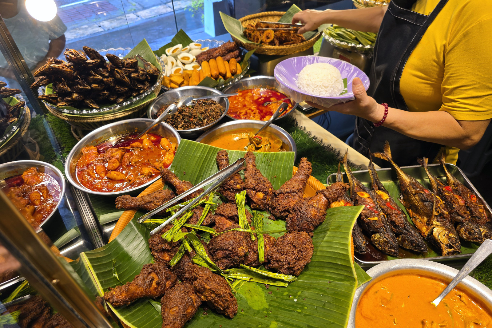 An appetizing Nasi Lemak selection showcasing spicy fried chicken, traditional curries, and fried fish served on banana leaves at a local food stall.