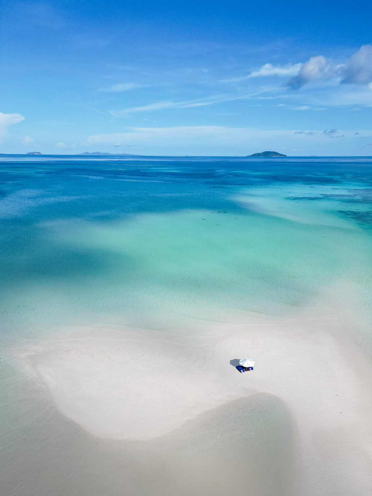 A tranquil beach setup on a pristine white sandbar at Amanpulo, surrounded by clear turquoise waters.