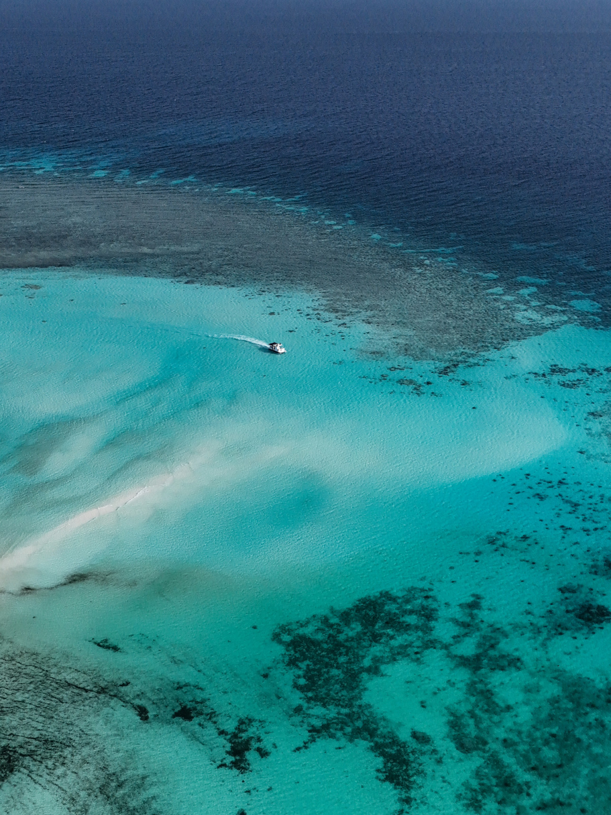 A boat skims over the turquoise waters and coral formations of Amanpulo.