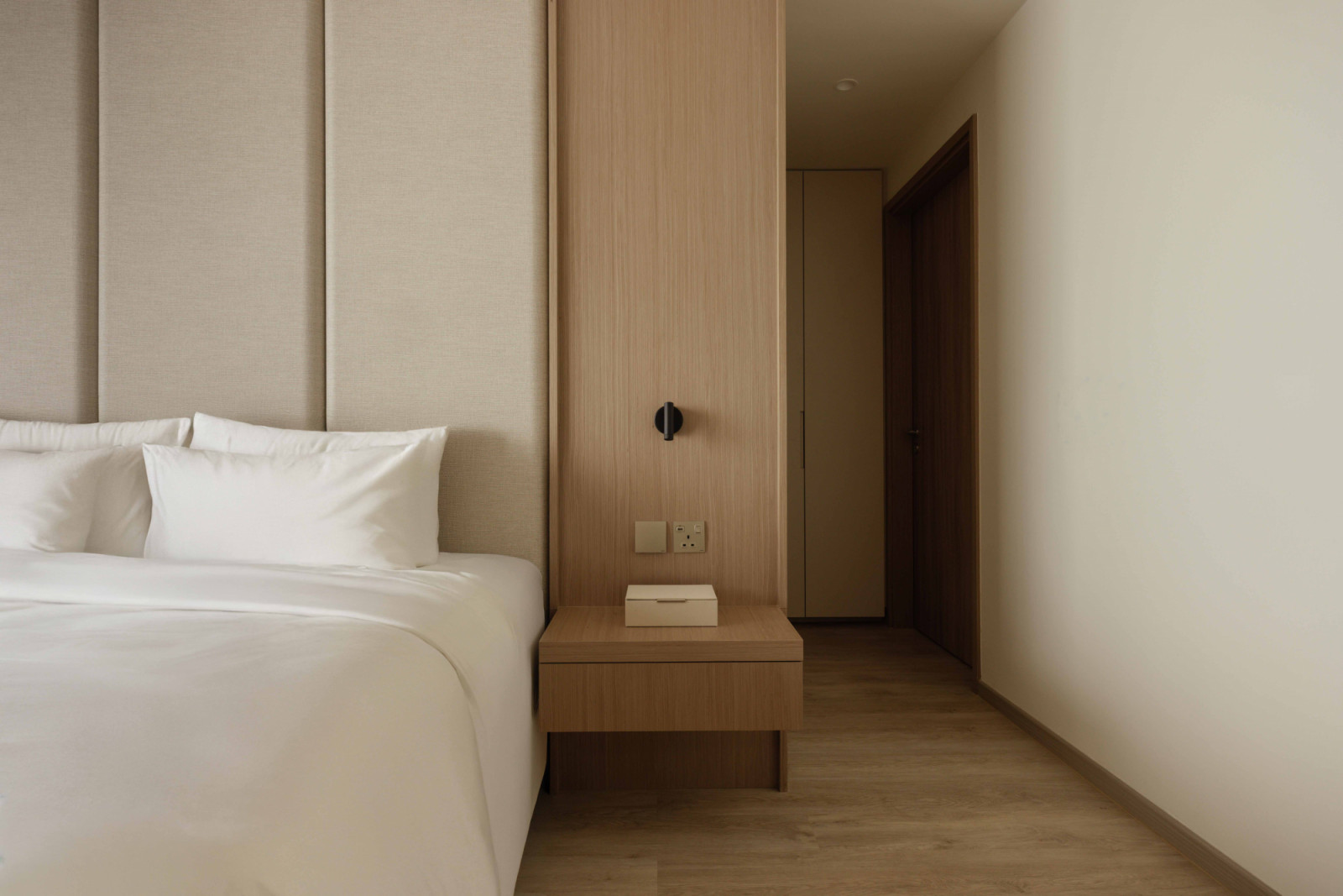 A floating oak nightstand sits beneath the panelled headboard wall