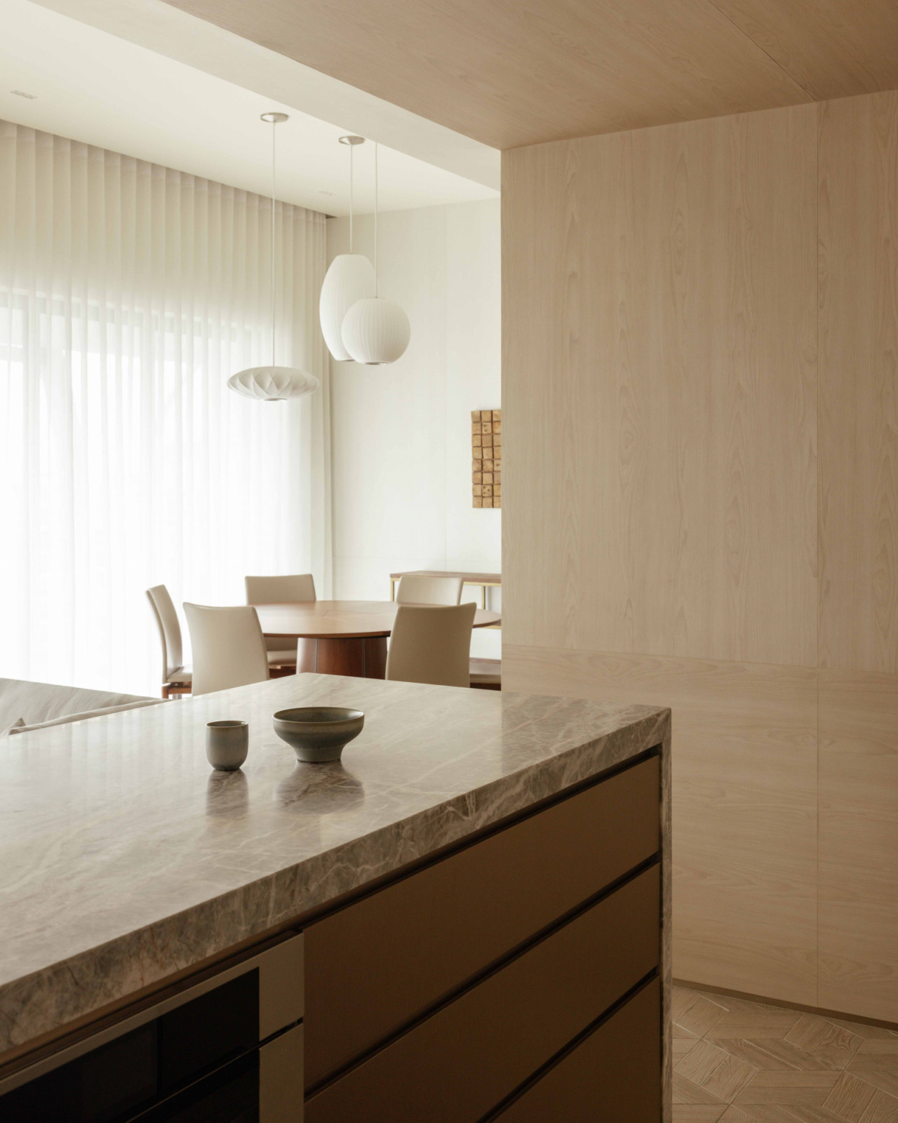 The marble island frames a glimpse into the dining area, softly lit by paper pendant lamps