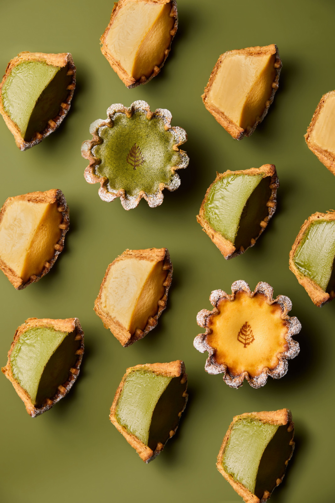 Matcha and custard tarts, some featuring a subtle tree emblem, offer a refined sweet finish to a meal.