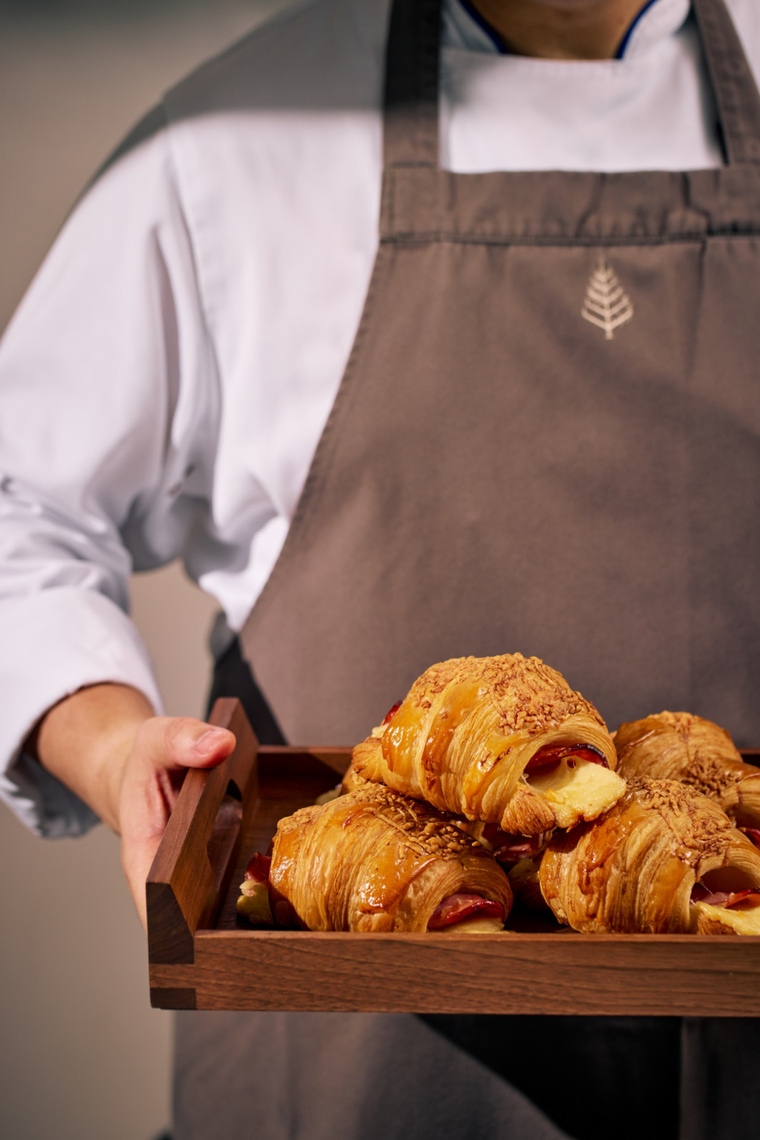 Savory ham and cheese croissants, fresh from the kitchen, are served by a chef on a bespoke wooden tray.
