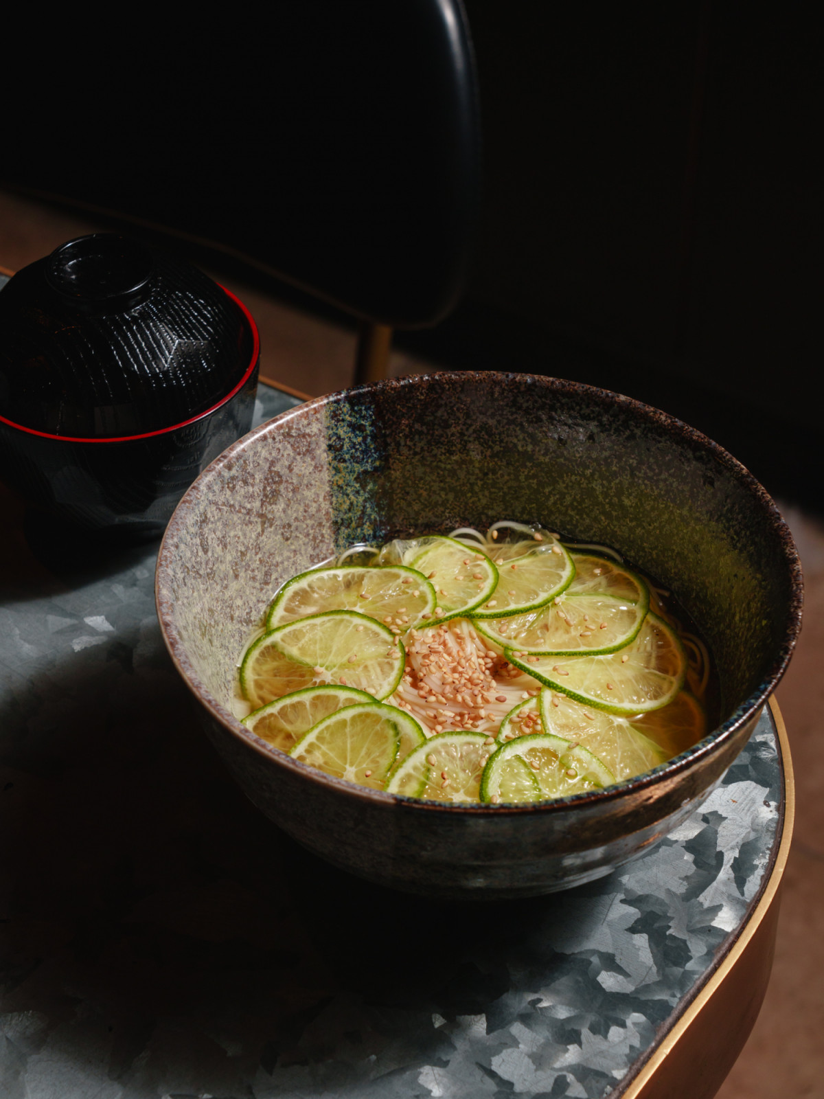 Japanese somen noodles with fresh sudachi lime slices and sesame seeds, served alongside a black lacquer bowl.