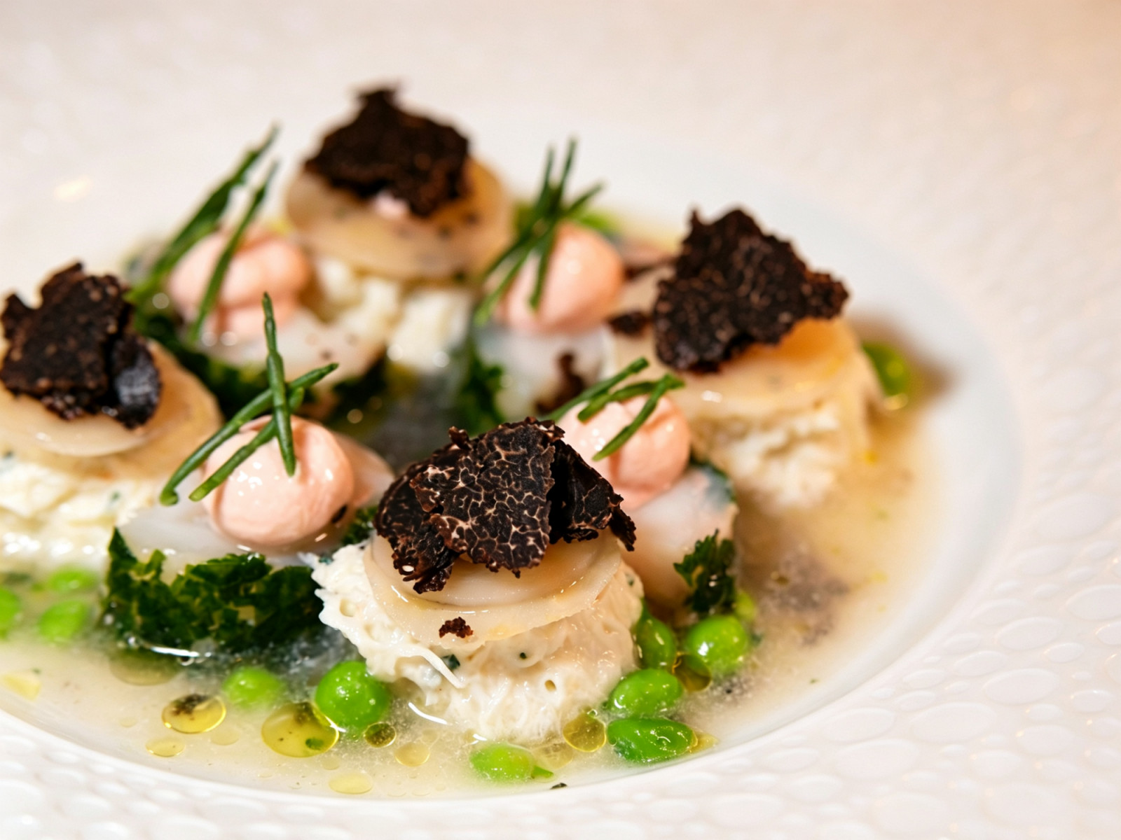 A plated dish featuring delicate seafood, generous black truffle shavings and bright green peas by Arcane.